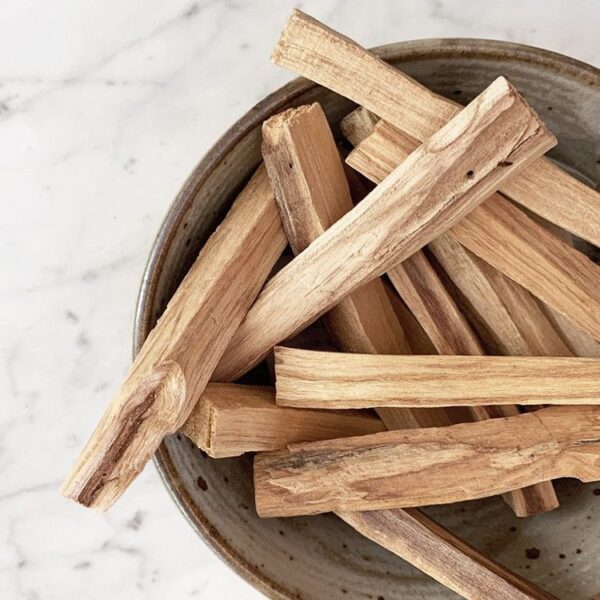Palitos de palo santo en un cuenco de cerámica sobre mármol blanco
