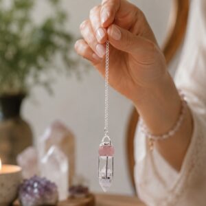 Péndulo con esfera de cuarzo rosa y punta de cuarzo transparente dentro de una jaula de varillas plateadas, colgado de una cadena