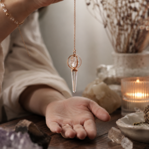 Péndulo con estrella Merkaba transparente dentro de dos aros cruzados de tono cobre y punta facetada de cuarzo, colgado de una cadena color cobre