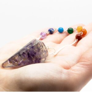 Péndulo de orgonita con lascas de amatista en resina transparente y cadena de siete cuentas de colores, sobre la palma de una mano