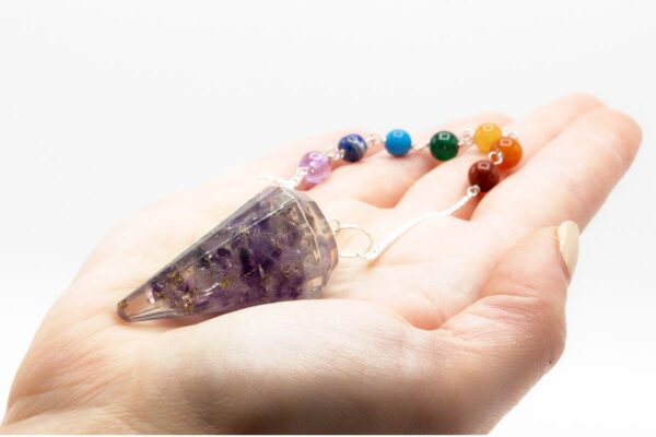 Péndulo de orgonita con lascas de amatista en resina transparente y cadena de siete cuentas de colores, sobre la palma de una mano