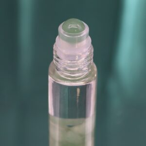 Envase verde de perfume roll-on con la carta de El Mago en dorado y el frasco de aventurina verde en la ventana