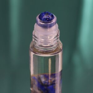 Envase azul de perfume roll-on con El Sol del tarot en dorado y el frasco de sodalita en la ventana