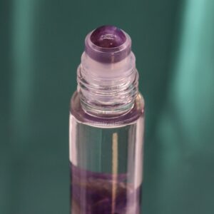Envase morado de perfume roll-on con La Luna del tarot en dorado, dos lobos aullando y el frasco de amatista en la ventana
