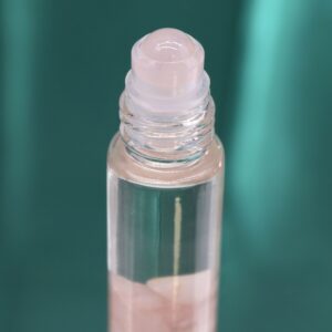 Envase rosa de perfume roll-on con la carta de Los Amantes en dorado y trocitos de cuarzo rosa