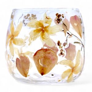 Portavelas pequeño de vidrio transparente con flores prensadas de color crema y pétalos rosados