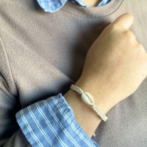 Pulsera de la amistad de cordón beige trenzado con una concha de cauri, en la muñeca; se envía una, de color al azar