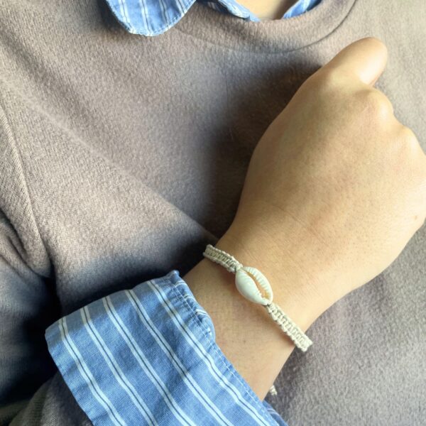 Pulsera de la amistad de cordón beige trenzado con una concha de cauri, en la muñeca; se envía una, de color al azar