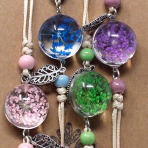 Dos pulseras de cordón beige con una esfera de vidrio con flores secas azules y verdes y una hoja calada plateada