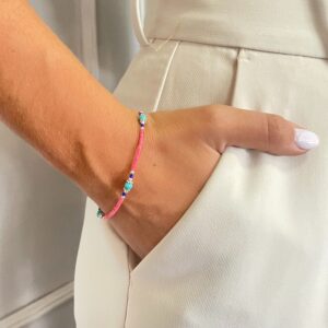 Pulsera de tubitos rosa coral con vetas oscuras y tres cuentas redondas color turquesa entre rondeles plateados, sobre fondo blanco