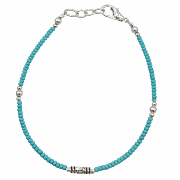 Pulsera fina de cuentas diminutas color turquesa con un tubito metálico grabado en el centro, mosquetón y cadenita, sobre fondo blanco