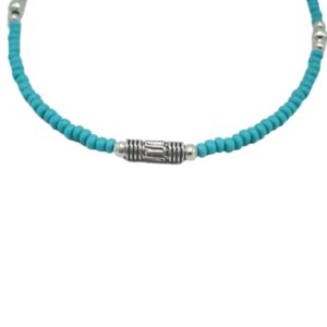 Pulsera fina de cuentas diminutas color turquesa con un tubito metálico grabado en el centro, mosquetón y cadenita, sobre fondo blanco
