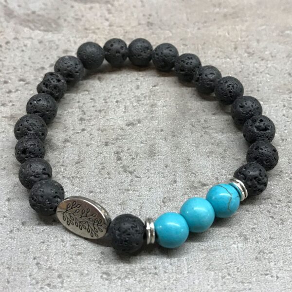 Pulsera elástica de cuentas de lava negra con tres cuentas de howlita color turquesa y una chapa ovalada con una hoja grabada