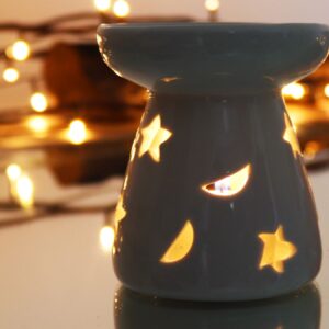 Quemador de aceite pequeño de cerámica blanca con medias lunas y estrellas caladas, sobre fondo blanco