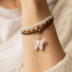 Set de tres pulseras elásticas en azul agua, melocotón y marrón dorado; la de ojo de tigre lleva una mariposa de tono plateado