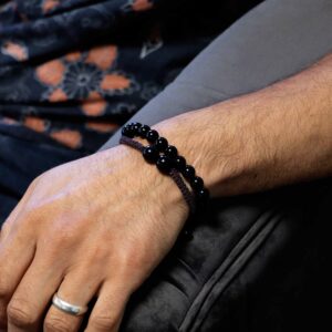 Pulsera elástica de cuentas de ágata negra y pulsera de cordón rojo trenzado con dos cuentas negras, sobre su tarjeta