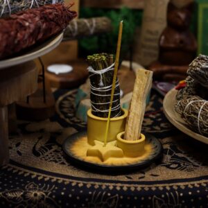 Soporte de cerámica en tono mostaza con dos cilindros y una estrella portaincienso sobre un plato con relieve de pétalos