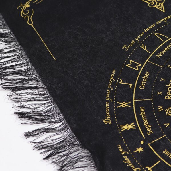 Detalle de tela de algodón negro con flecos y una rueda de runas y meses estampada en tono dorado