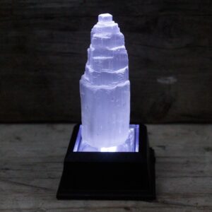Torre de selenita blanca natural de 10 cm tallada en escalones, sobre una mesa de madera con hiedra