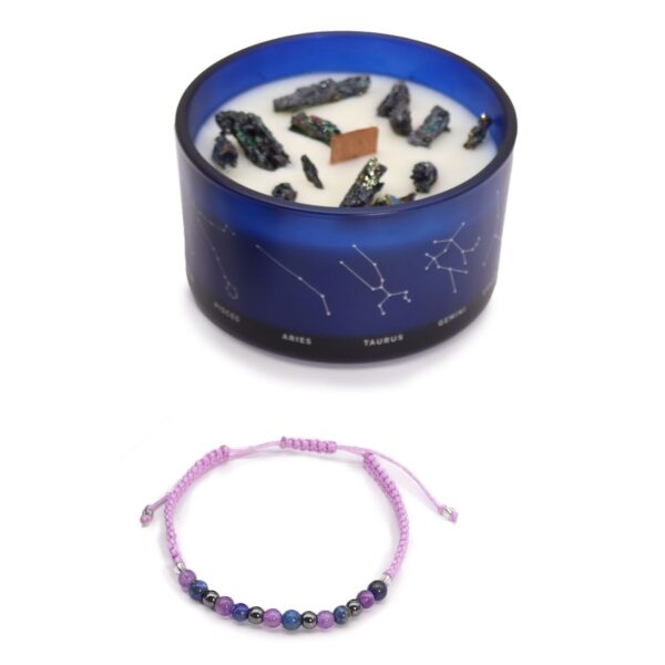 Vela de soja en vaso azul con constelaciones y trozos de pirita, junto a una pulsera de cordón lila con cuentas de amatista, lapislázuli y hematites