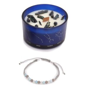 Vela de soja en vaso azul con constelaciones y trozos de pirita, junto a una pulsera de cordón gris claro con cuentas de aguamarina, cuarzo ahumado y piedra luna
