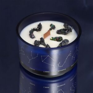 Vela de soja en vaso azul con constelaciones y trozos de pirita, junto a una pulsera de cordón gris claro con cuentas de aguamarina, cuarzo ahumado y piedra luna
