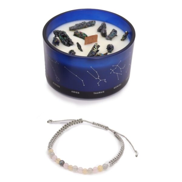 Vela de soja en vaso azul con constelaciones y trozos de pirita, junto a una pulsera de cordón gris claro con cuentas amarillas, rosas y blancas