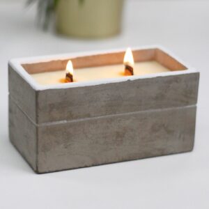 Vela rectangular en caja de hormigón gris con dos mechas de madera encendidas