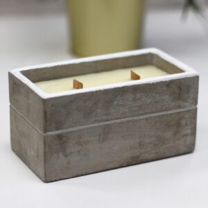 Vela rectangular en caja de hormigón gris con dos mechas de madera encendidas