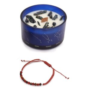 Vela de soja en vaso azul con constelaciones y trozos de pirita, junto a una pulsera de cordón rojo teja con cuentas de ojo de tigre y cornalina