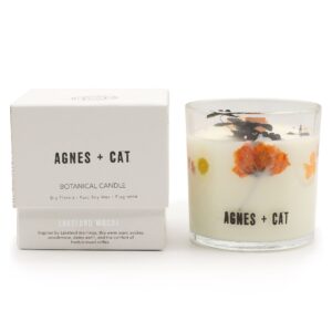 Vela de soja en vaso de vidrio con flores secas naranjas y hojas negras junto a su caja blanca