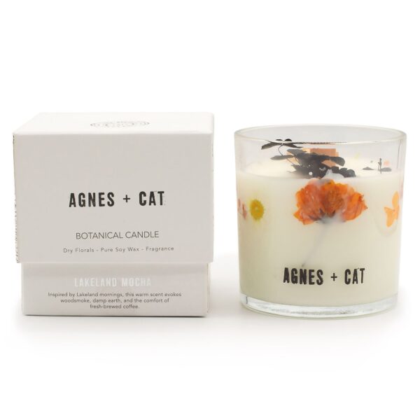 Vela de soja en vaso de vidrio con flores secas naranjas y hojas negras junto a su caja blanca