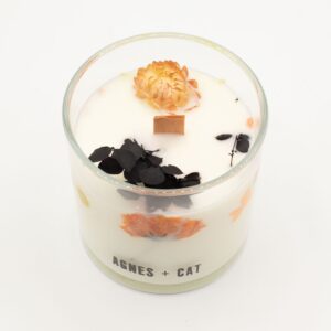 Vela de soja en vaso de vidrio con flores secas naranjas y hojas negras junto a su caja blanca