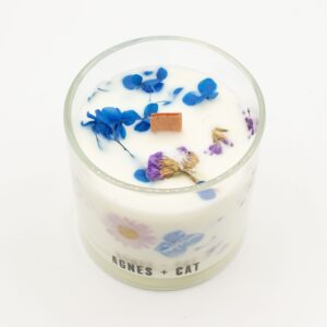 Vela de soja en vaso de vidrio con flores secas azules y lilas junto a su caja blanca