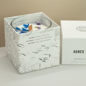 Vela de soja en vaso de vidrio con flores secas azules y lilas junto a su caja blanca