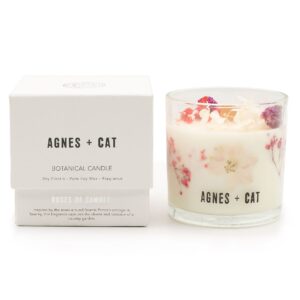 Vela de soja en vaso de vidrio con flores secas rosas y moradas junto a su caja blanca