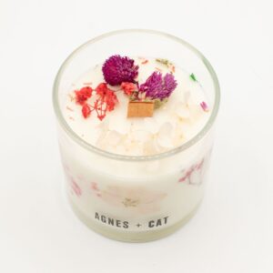 Vela de soja en vaso de vidrio con flores secas rosas y moradas junto a su caja blanca
