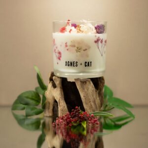 Vela de soja en vaso de vidrio con flores secas rosas y moradas junto a su caja blanca