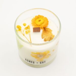 Vela de soja en vaso de vidrio con flores secas amarillas y helecho junto a su caja blanca