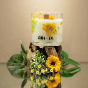 Vela de soja en vaso de vidrio con flores secas amarillas y helecho junto a su caja blanca