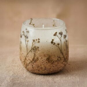 Vela en tarro de vidrio esmerilado blanco y arena con ramitas de flores silvestres secas incrustadas